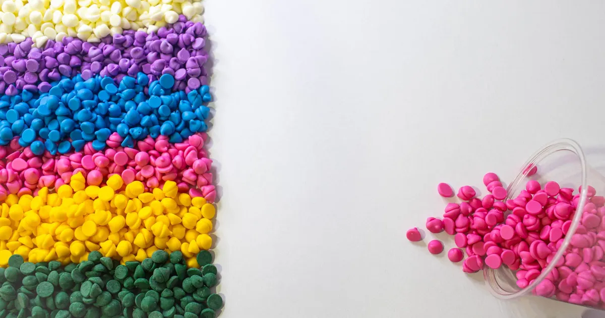 Black PEEK vs natural PEEK colour: rows of coloured plastic pellets in purple, blue, yellow and green on a white surface