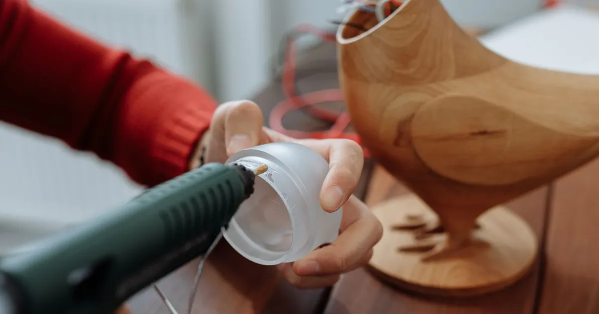Bonding PEEK needs the right adhesive: a hot glue gun applying adhesive to a clear plastic lid held in a hand