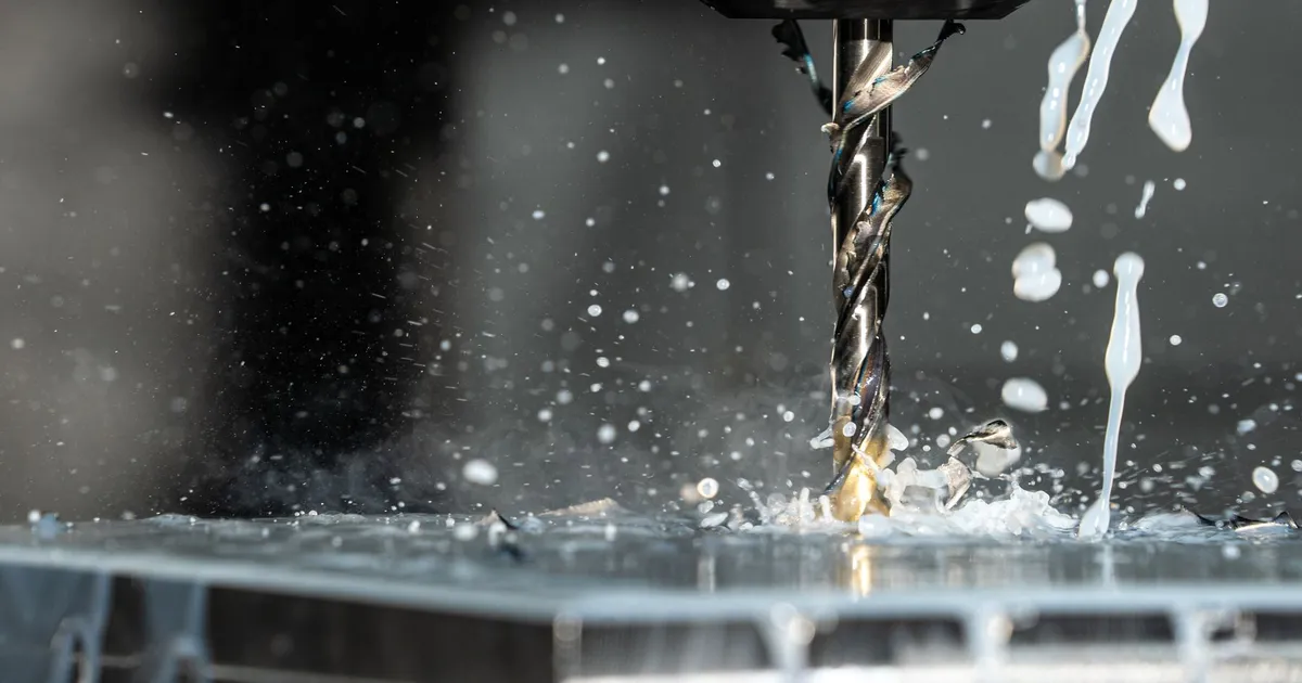 Drilling PEEK with coolant: a twist drill bit cutting into a block while coolant splashes around the hole
