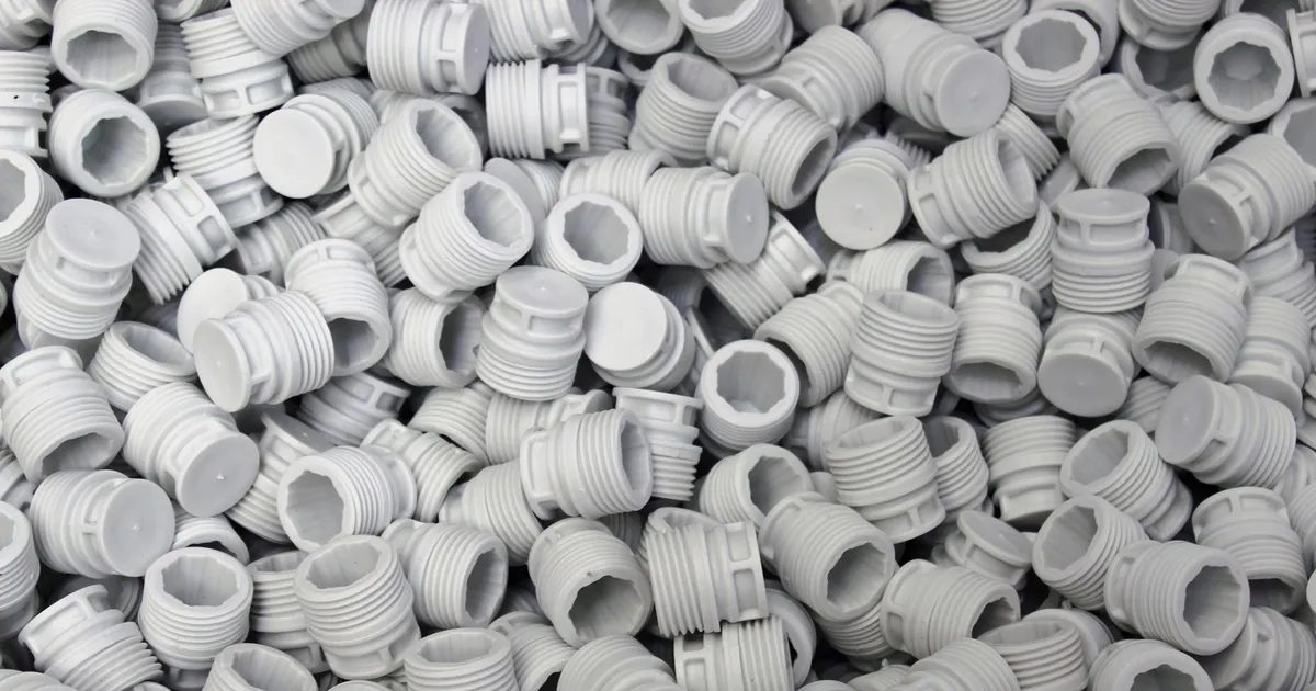 PEEK injection molding vs machining: bulk white plastic threaded plugs in a pile