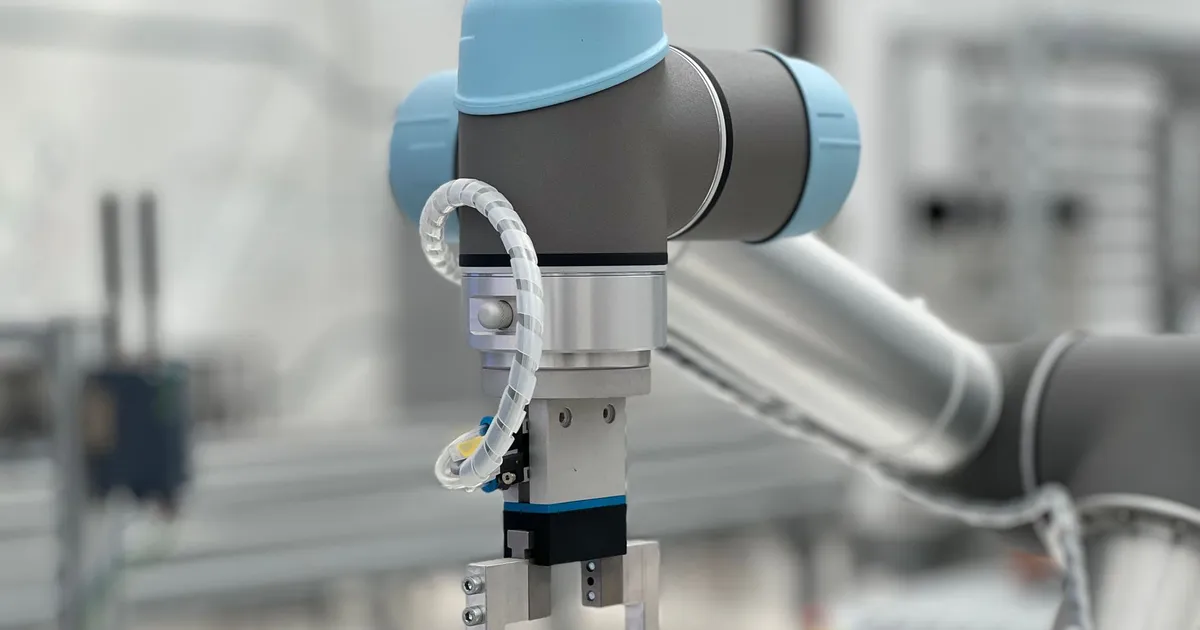 PEEK robot gripper fingers context: a collaborative robot arm with a two finger gripper holding in front of a blurred workshop