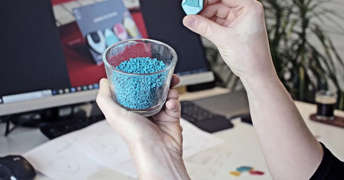 PEEK vs PEKK resin: a hand holding a glass of small blue plastic pellets and one pellet between the fingers